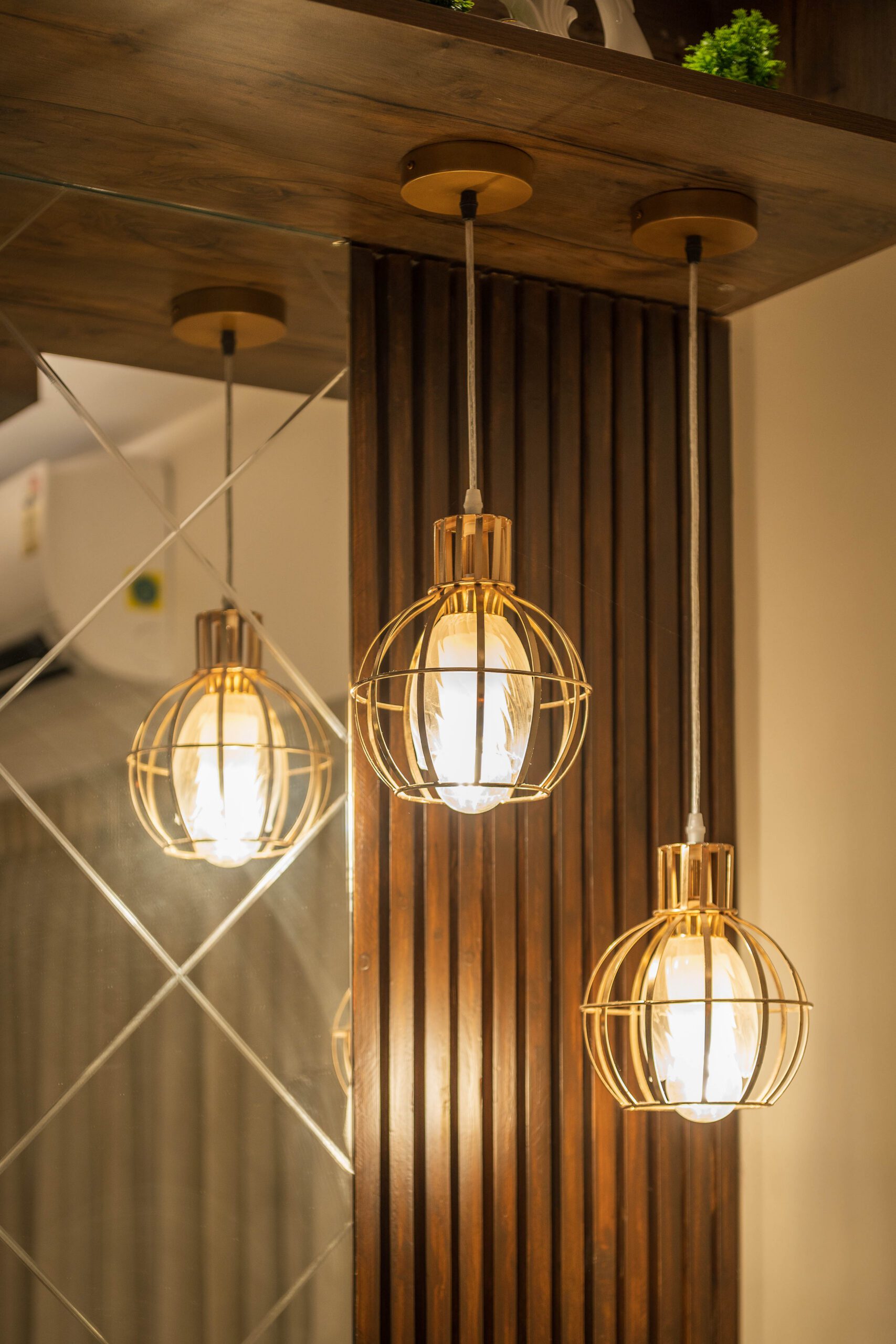 Close view of four amber glass pendant lights with exposed filament bulbs on black cords, hanging below a walnut ceiling raft over the dining table at Brigade Woods, Bangalore