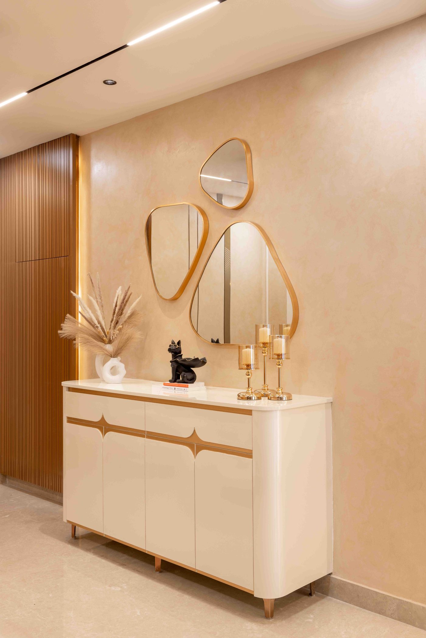 Entry console in white with a slim gold framed arched mirror above it and sculptural objects, in a completed home at Auro Kohinoor, Hyderabad