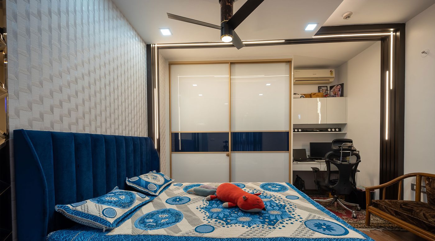 Bedroom with a bold blue geometric painted feature wall, an upholstered bed with a deep padded headboard, full-length curtains and warm bedside lighting, in a completed home at Mahindra Windchimes, Bangalore