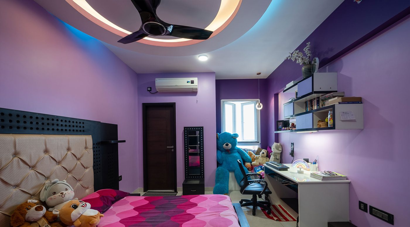 Child's bedroom at Mahindra Windchimes, Bangalore, in lilac and purple, with a circular tiered cove ceiling lit in warm white and cyan, a wall mounted split air conditioner, a study desk and wall shelves