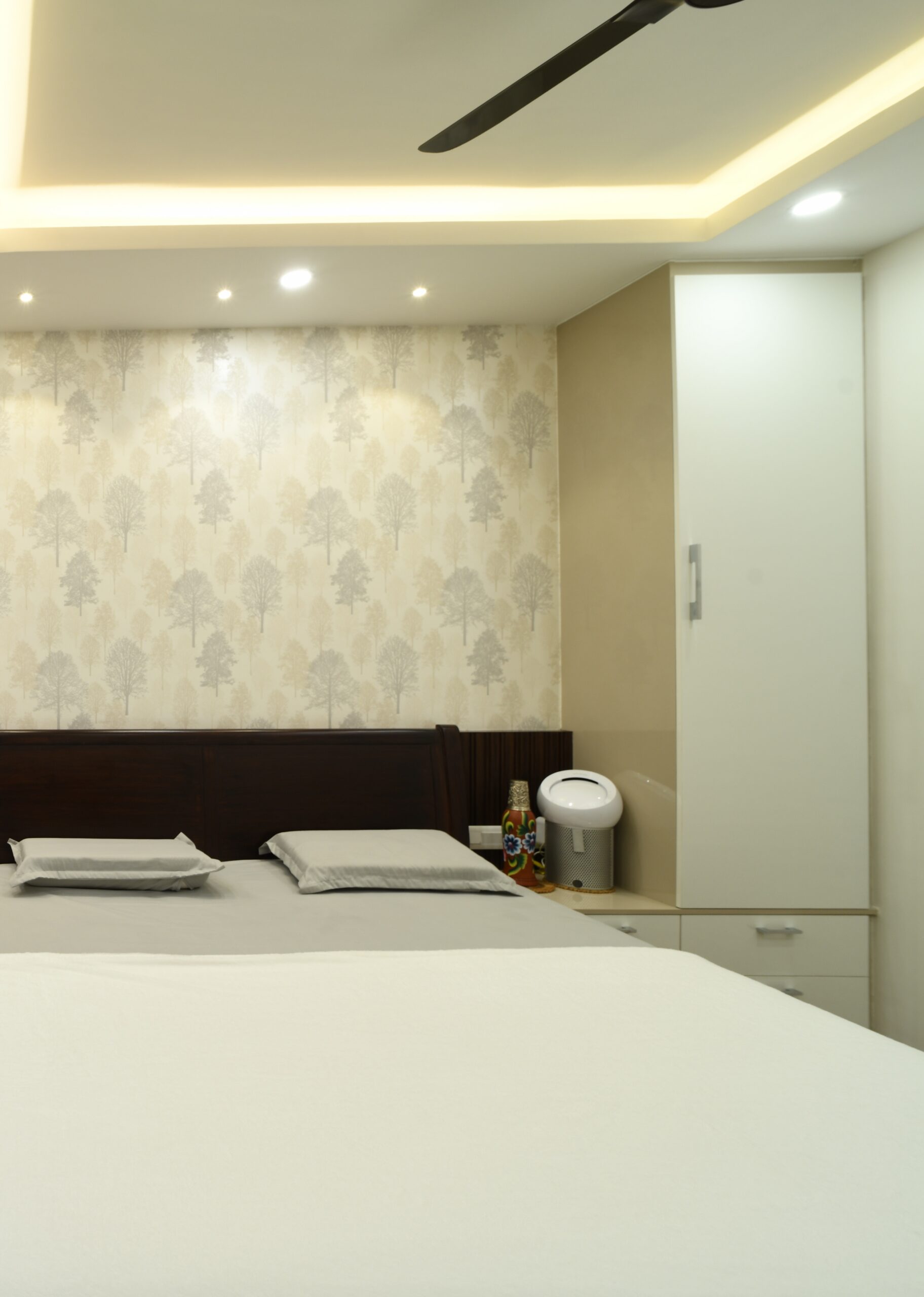 A bedroom in a Bangalore home with a botanical wallpaper feature wall and a dark wood headboard, designed by Furdo